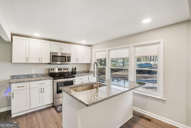 kitchen featuring appliances with stainless steel finishes, white cabinetry, a sink, and light stone countertops