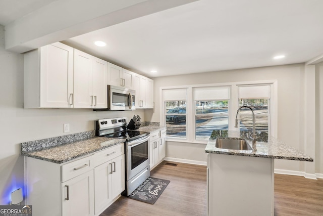 kitchen with stainless steel appliances, stone countertops, a sink, and light wood-style floors