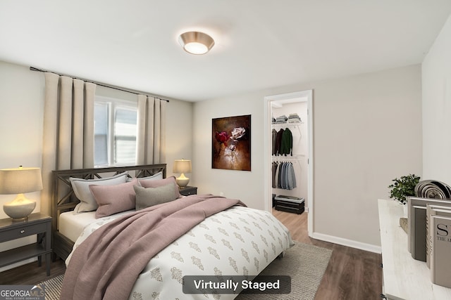 bedroom with a walk in closet, baseboards, dark wood finished floors, and a closet