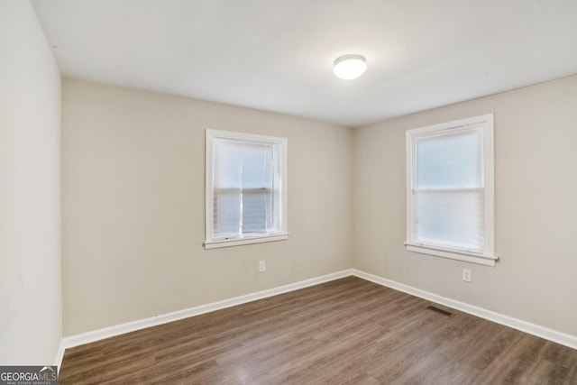 spare room featuring wood finished floors, visible vents, and baseboards