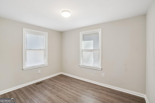 unfurnished room featuring baseboards, visible vents, and wood finished floors