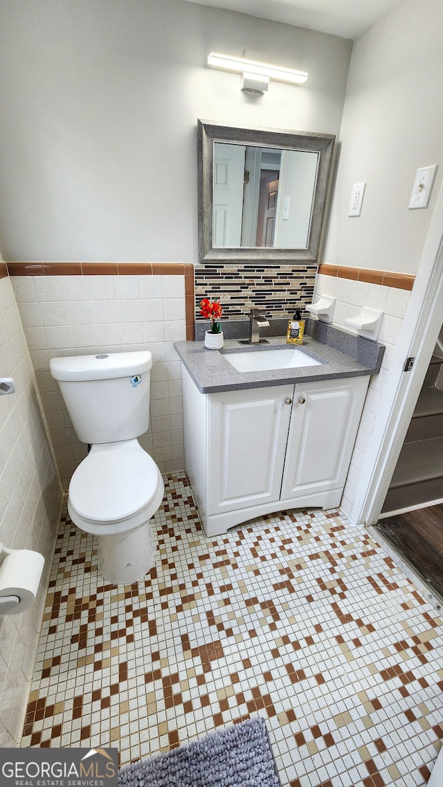 bathroom featuring toilet, a wainscoted wall, tile walls, and vanity