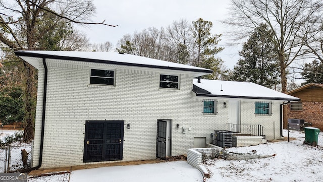 snow covered property featuring brick siding and fence