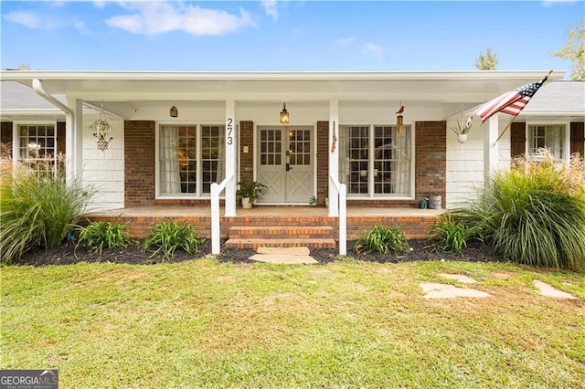 view of exterior entry with brick siding, covered porch, and a yard