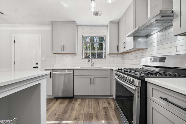 2111 Glenwood Downs Dr, Decatur, GA 30035 - kitchen featuring stainless steel appliances, gray cabinets, wall chimney range hood, crown molding, and light wood-style flooring