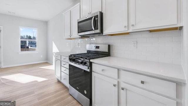 kitchen featuring stainless steel appliances, white cabinetry, light wood-style floors, and decorative backsplash