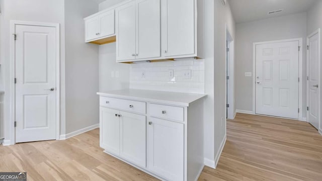 kitchen with visible vents, decorative backsplash, light countertops, light wood-style floors, and white cabinetry