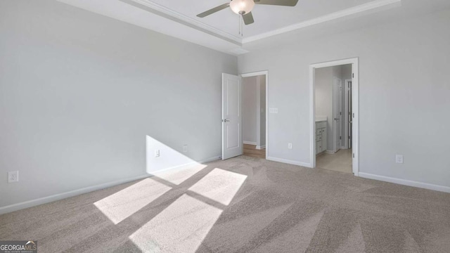 unfurnished bedroom featuring crown molding, a raised ceiling, light colored carpet, connected bathroom, and baseboards