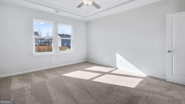 carpeted spare room with a ceiling fan, a raised ceiling, visible vents, and baseboards