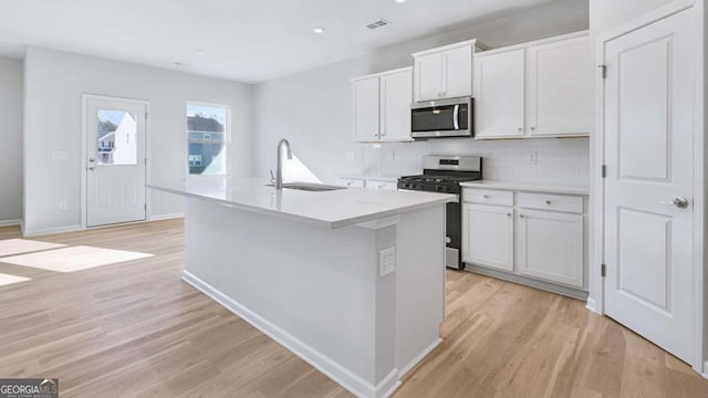 kitchen featuring a center island with sink, visible vents, light wood-style flooring, appliances with stainless steel finishes, and a sink