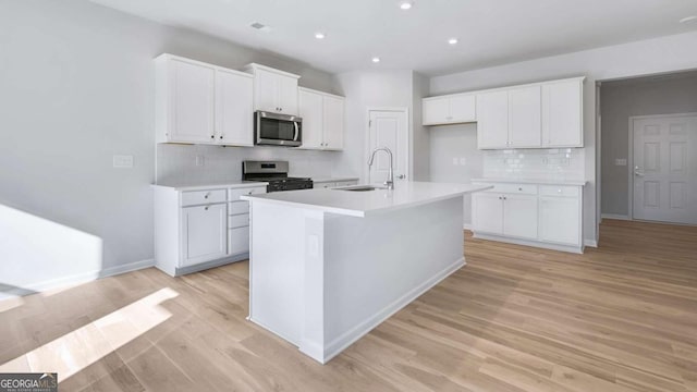 kitchen featuring a sink, white cabinets, appliances with stainless steel finishes, light wood-type flooring, and an island with sink