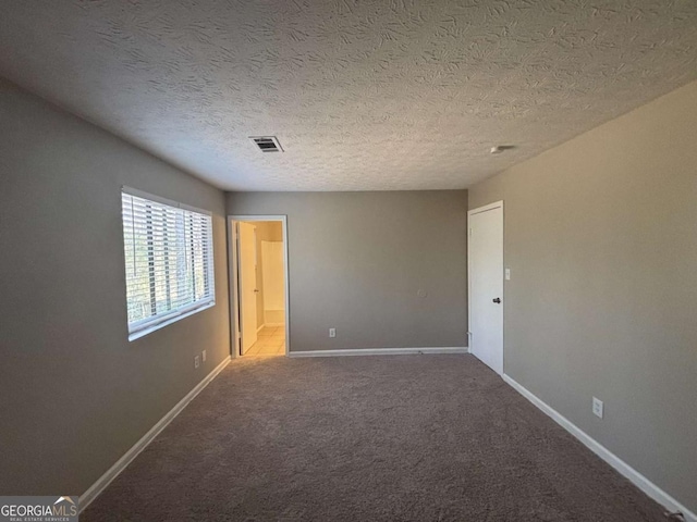 spare room with carpet floors, visible vents, a textured ceiling, and baseboards