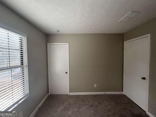 unfurnished bedroom with visible vents, a textured ceiling, carpet flooring, and multiple windows