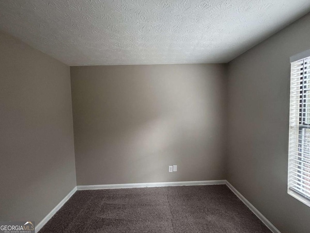 unfurnished room with a wealth of natural light, baseboards, a textured ceiling, and dark colored carpet