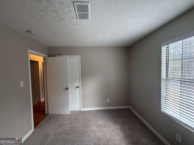 unfurnished bedroom with baseboards, visible vents, a textured ceiling, carpet flooring, and a closet