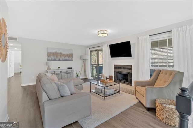 living room featuring a fireplace, wood finished floors, visible vents, and baseboards