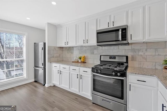 kitchen with backsplash, appliances with stainless steel finishes, light wood-style floors, white cabinetry, and light stone countertops