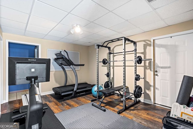 exercise area with a paneled ceiling, dark wood finished floors, and baseboards