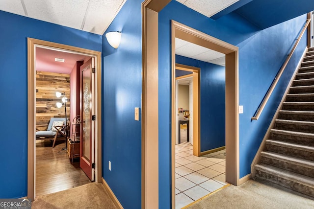 hallway featuring carpet flooring, wood walls, stairway, and baseboards