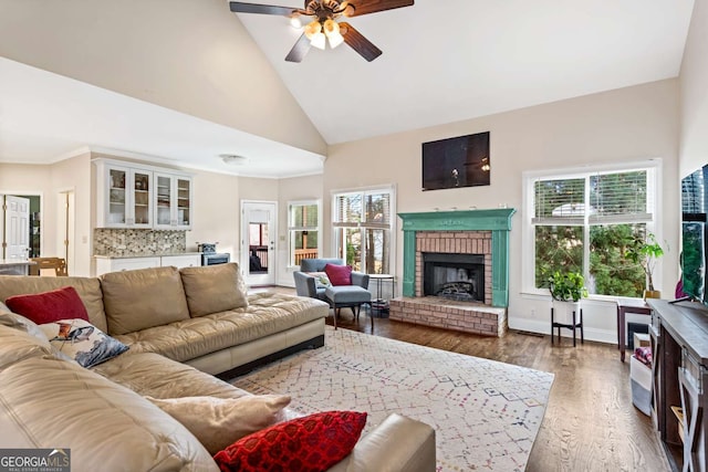 living room with a ceiling fan, wood finished floors, crown molding, a fireplace, and high vaulted ceiling