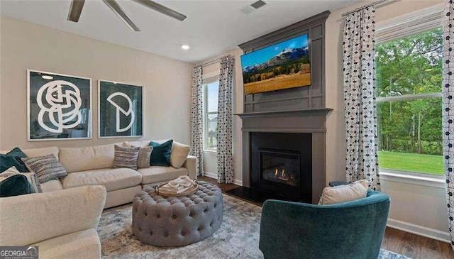 living room with baseboards, visible vents, a ceiling fan, a glass covered fireplace, and wood finished floors