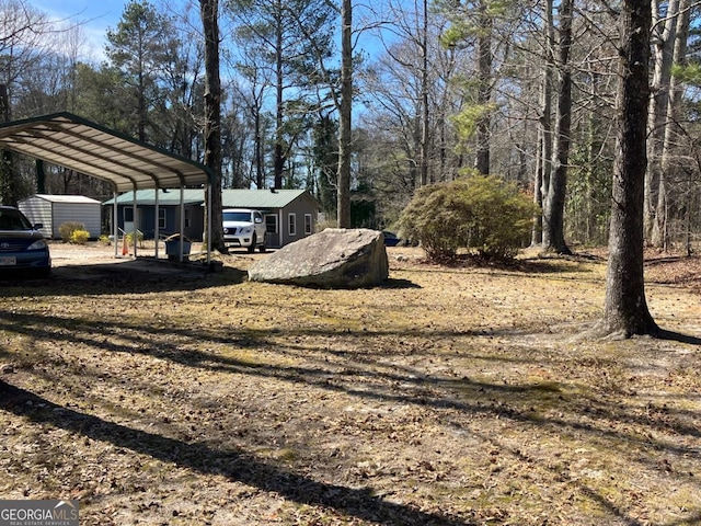 view of yard featuring dirt driveway, a storage unit, a carport, and an outbuilding