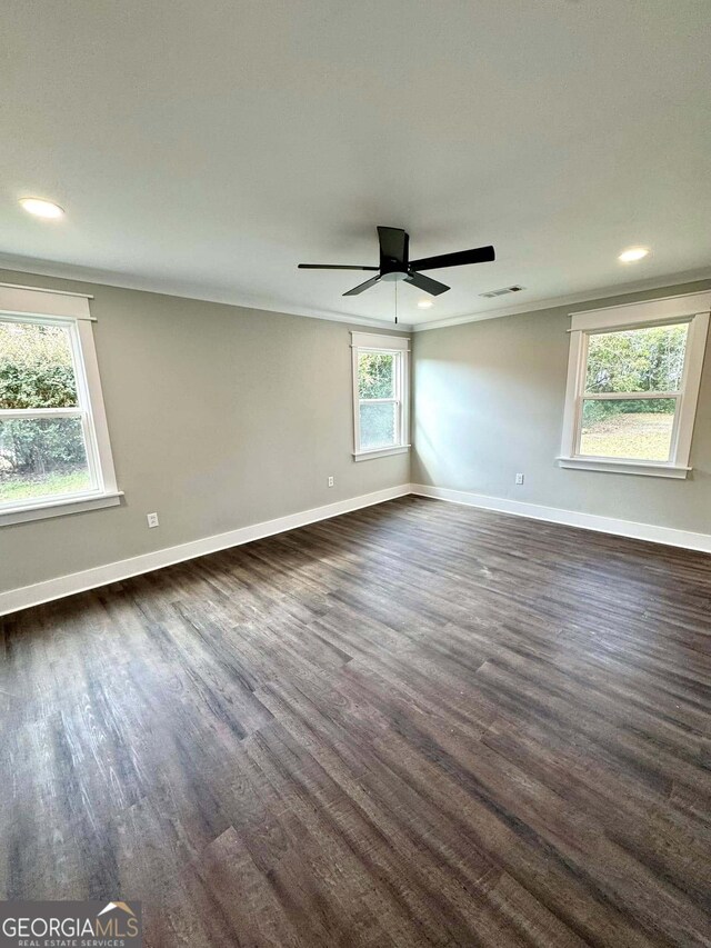 empty room with dark wood-style floors, baseboards, visible vents, and ornamental molding