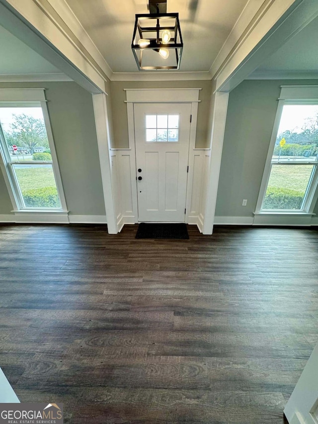 foyer with a wainscoted wall, ornamental molding, plenty of natural light, and dark wood finished floors