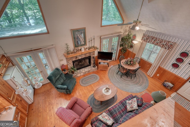 living room with french doors, a towering ceiling, ceiling fan, a stone fireplace, and wood finished floors