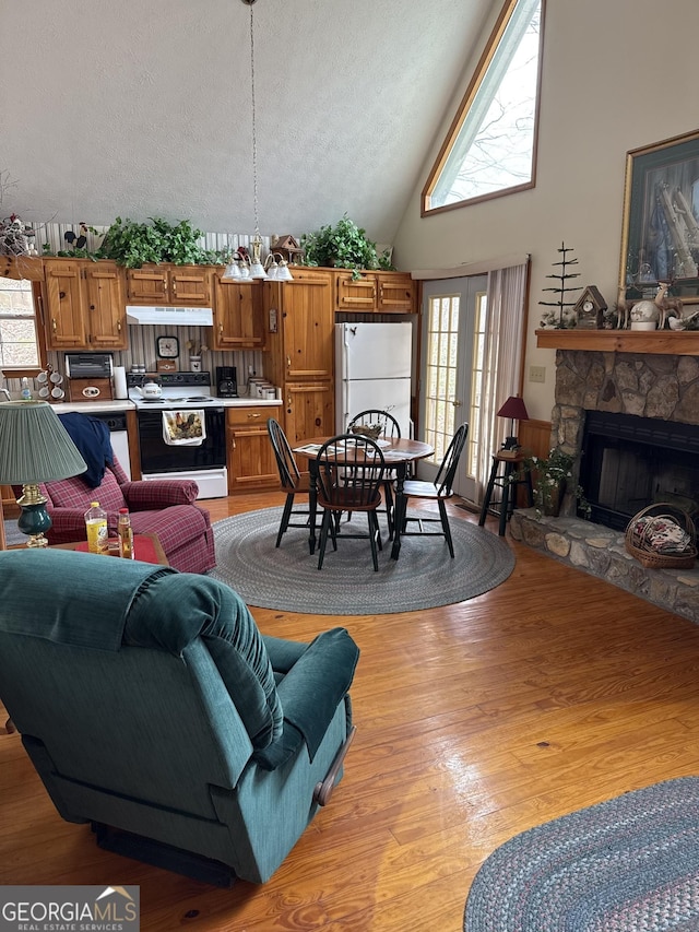 living area featuring french doors, a stone fireplace, a textured ceiling, high vaulted ceiling, and light wood-type flooring