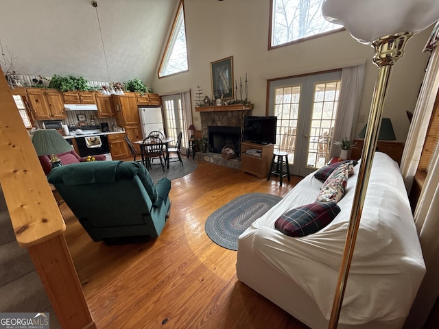 living area with a towering ceiling, light wood-style flooring, a fireplace, and french doors