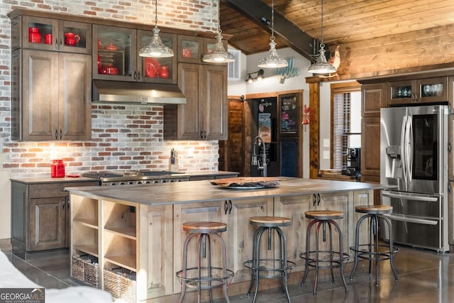 kitchen featuring brick wall, under cabinet range hood, butcher block countertops, appliances with stainless steel finishes, and wooden ceiling