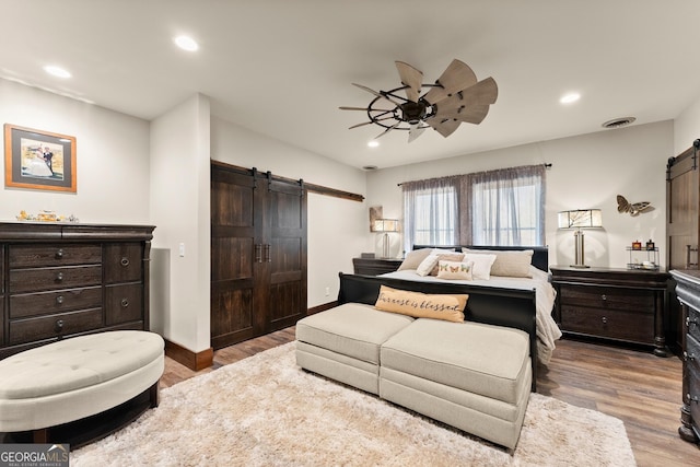 bedroom with recessed lighting, a barn door, and wood finished floors