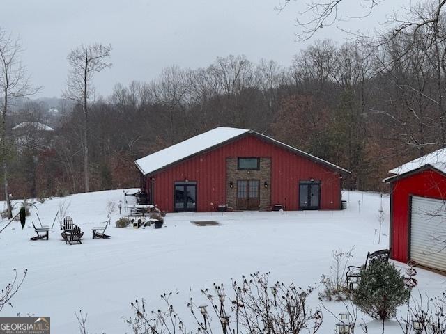 snow covered structure featuring a forest view and an outdoor structure