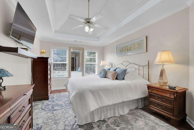 bedroom with ornamental molding, a tray ceiling, baseboards, and wood finished floors