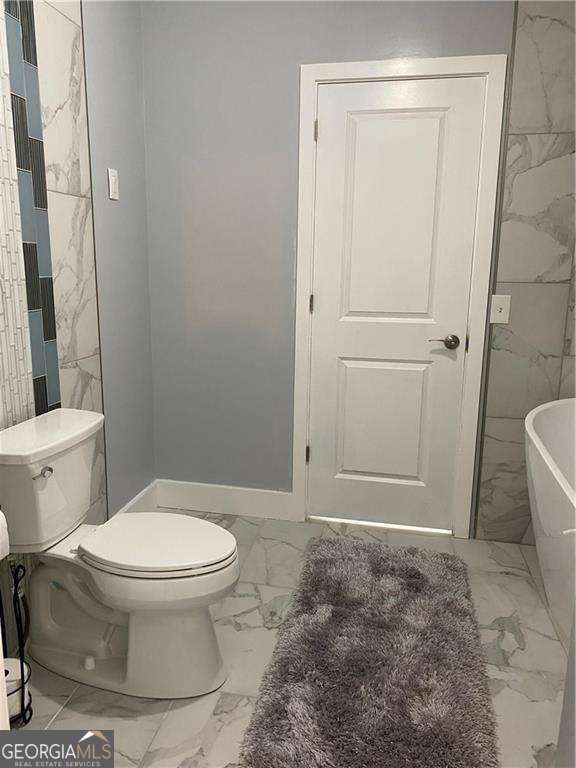 bathroom featuring marble finish floor, a freestanding bath, and toilet