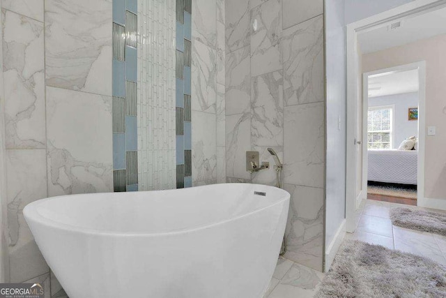 full bath featuring marble finish floor, tile walls, a freestanding tub, and connected bathroom