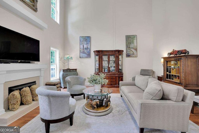 living area featuring a towering ceiling, a fireplace with raised hearth, and wood finished floors