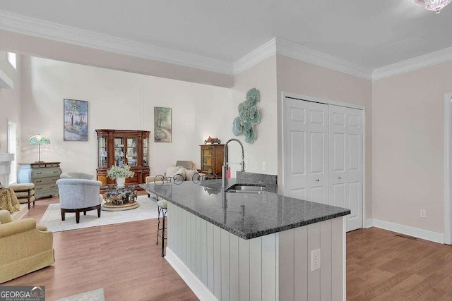 kitchen with a breakfast bar, wood finished floors, a sink, ornamental molding, and dark stone countertops