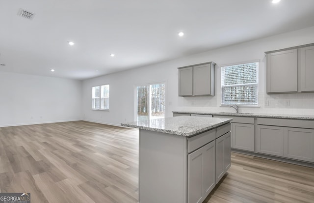 kitchen with visible vents, decorative backsplash, a center island, gray cabinets, and a sink