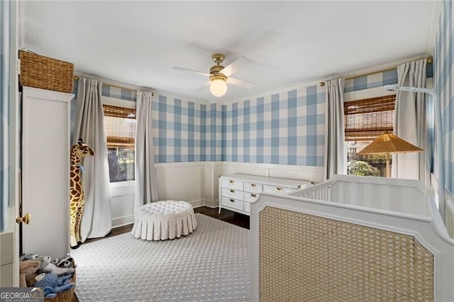 unfurnished bedroom featuring a wainscoted wall, dark wood finished floors, a ceiling fan, and wallpapered walls