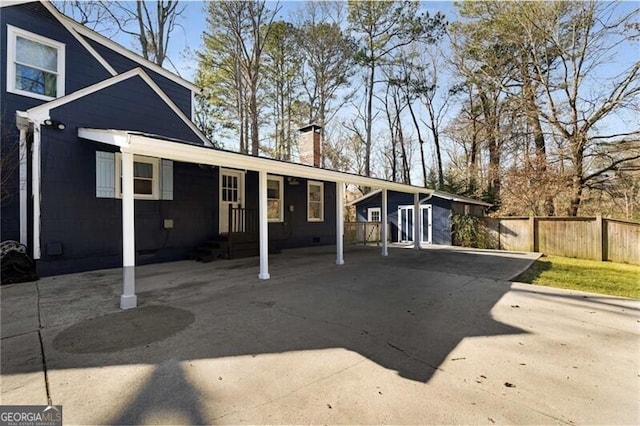 rear view of house with a carport, concrete driveway, fence, and a chimney