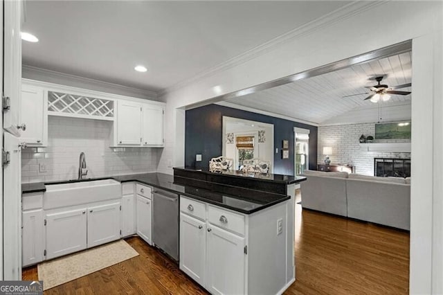 kitchen with a peninsula, a sink, white cabinetry, stainless steel dishwasher, and dark countertops