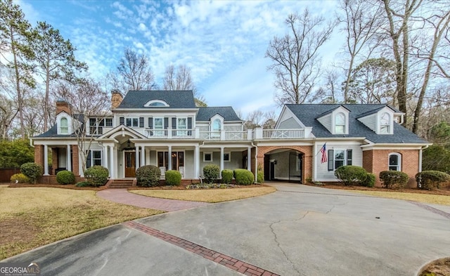 view of front facade featuring driveway, brick siding, a front lawn, and a balcony