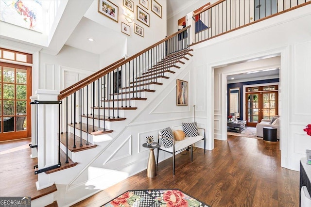 stairs featuring a decorative wall, wood finished floors, a towering ceiling, french doors, and crown molding