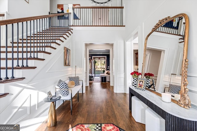 entrance foyer with a towering ceiling, dark wood-style floors, and stairs