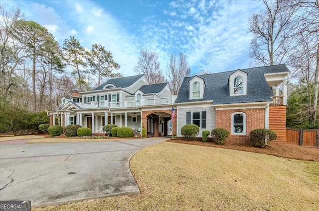 view of front of house with a balcony, brick siding, a shingled roof, fence, and driveway