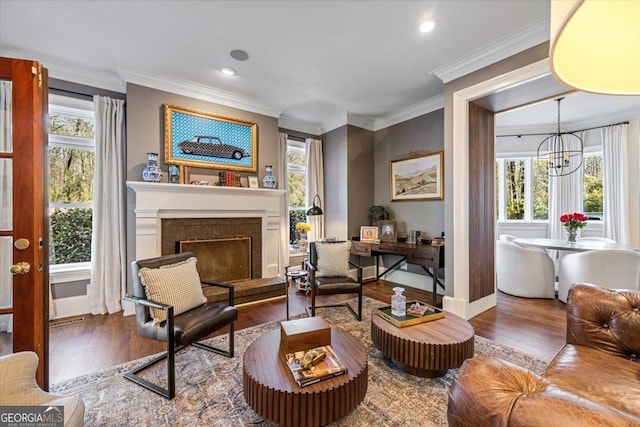 living area featuring recessed lighting, a fireplace with raised hearth, ornamental molding, wood finished floors, and a chandelier