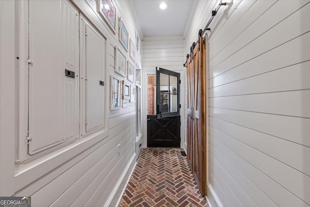 hall with brick floor, recessed lighting, wood walls, and a barn door