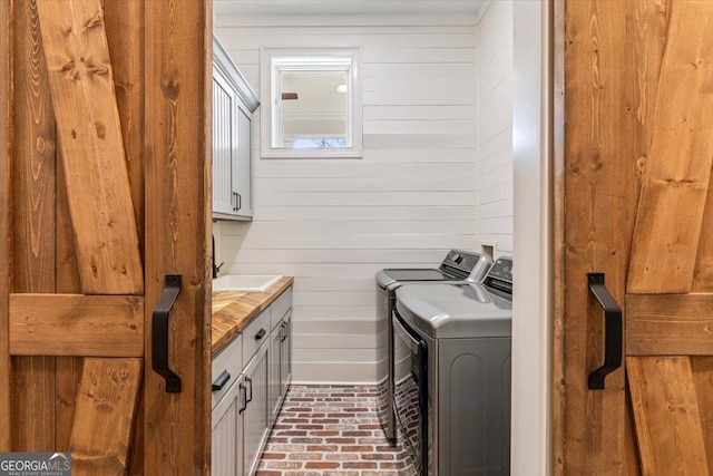 clothes washing area with brick floor, washing machine and clothes dryer, cabinet space, and wooden walls